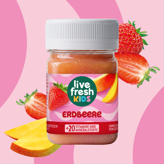 LiveFresh Kids Erdbeere im Glas vor rosa Hintergrund mit Erdbeeren und Mangostücken. Auf dem Etikett steht "live fresh KIDS". "ERDBEERE" und "+20 VITAMINE UND MINERALSTOFFE".