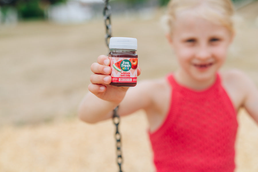 Mädchen präsentiert einen LiveFresh Kids Shot Wassermelone auf einem Spielplatz.