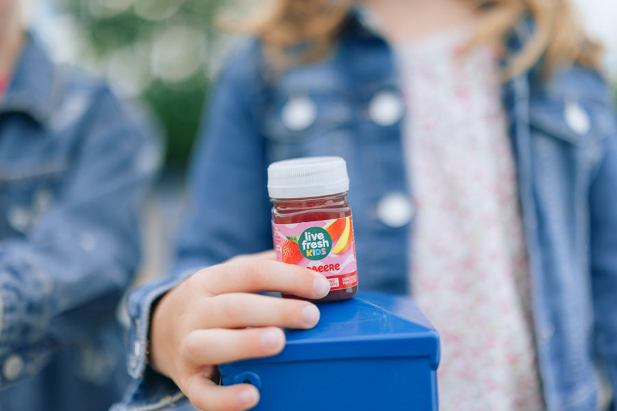 Nahaufnahme eines LiveFresh Kids Shots Erdbeere vor einem Mädchen in Jeansjacke.