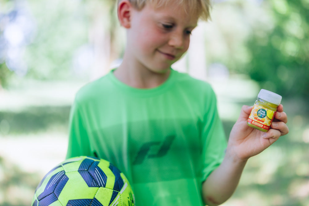 Junge mit Fußball hält einen LiveFresh Kids Shot Orange in der Hand.