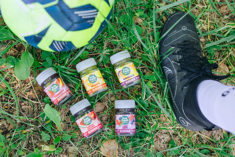 Fünf LiveFresh Kids Shots liegen neben einem Fußballschuh und Fußball im Gras.